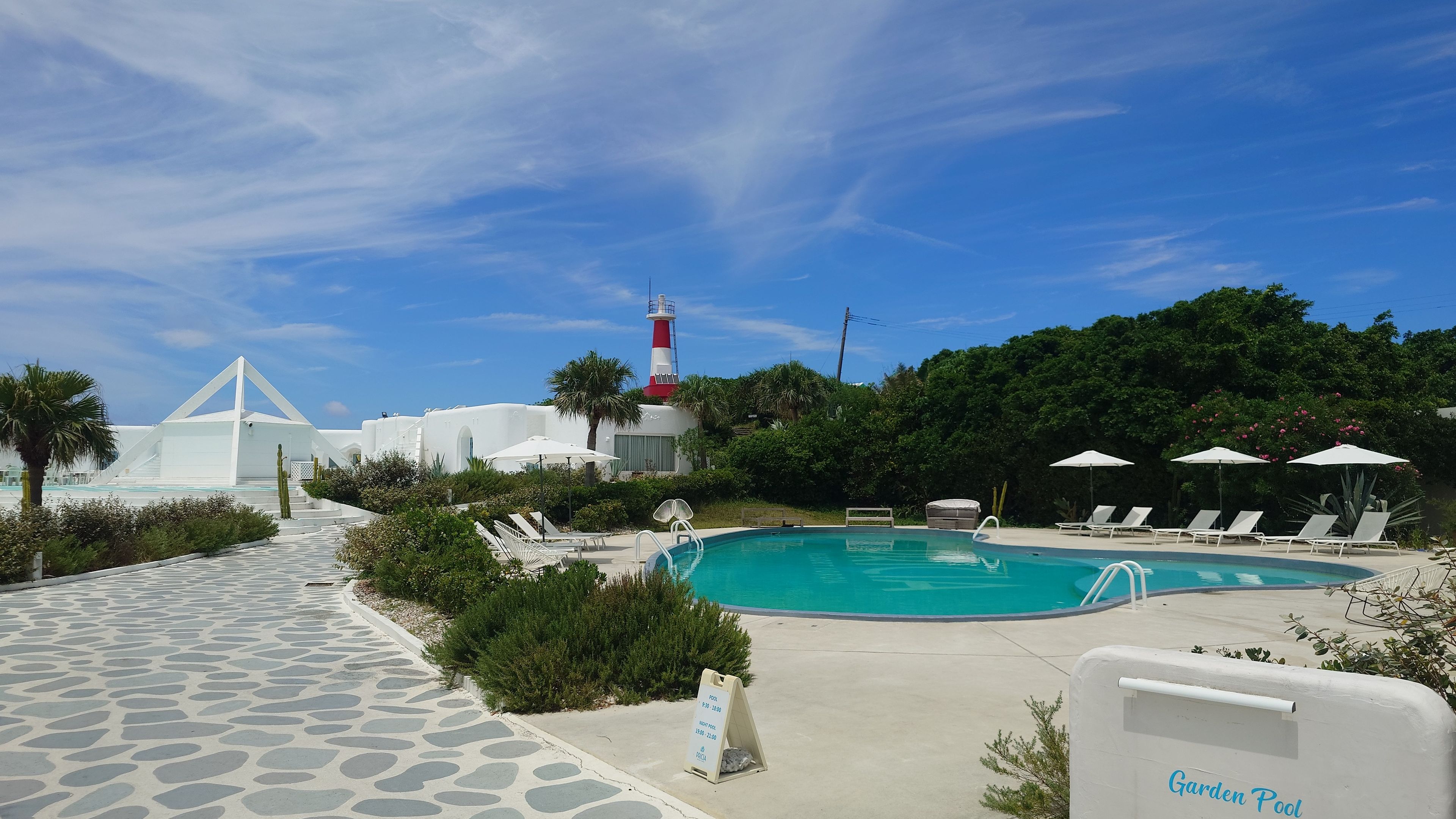 Spacious outdoor swimming pool at Pricia Resort Yoron, lined with sun loungers and umbrellas.