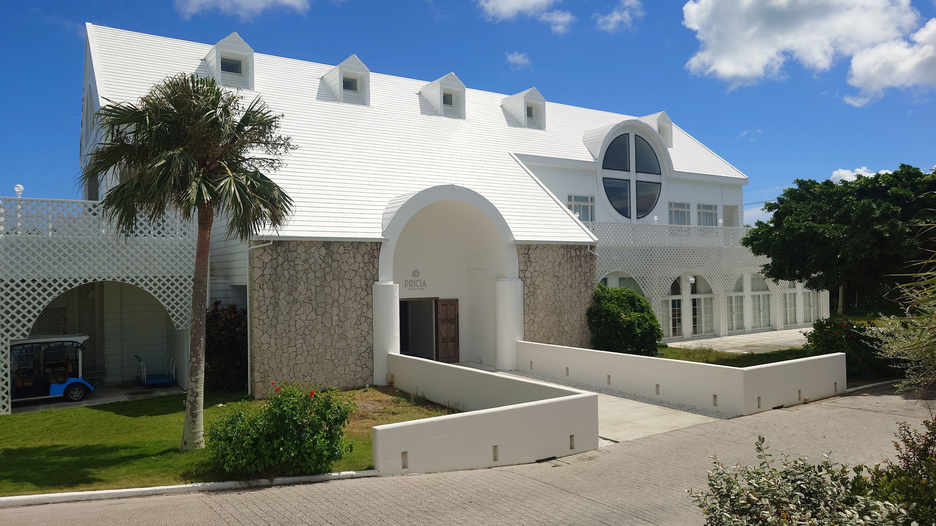 Exterior of the main reception building at Pricia Resort Yoron, surrounded by white structures and tropical plants.
